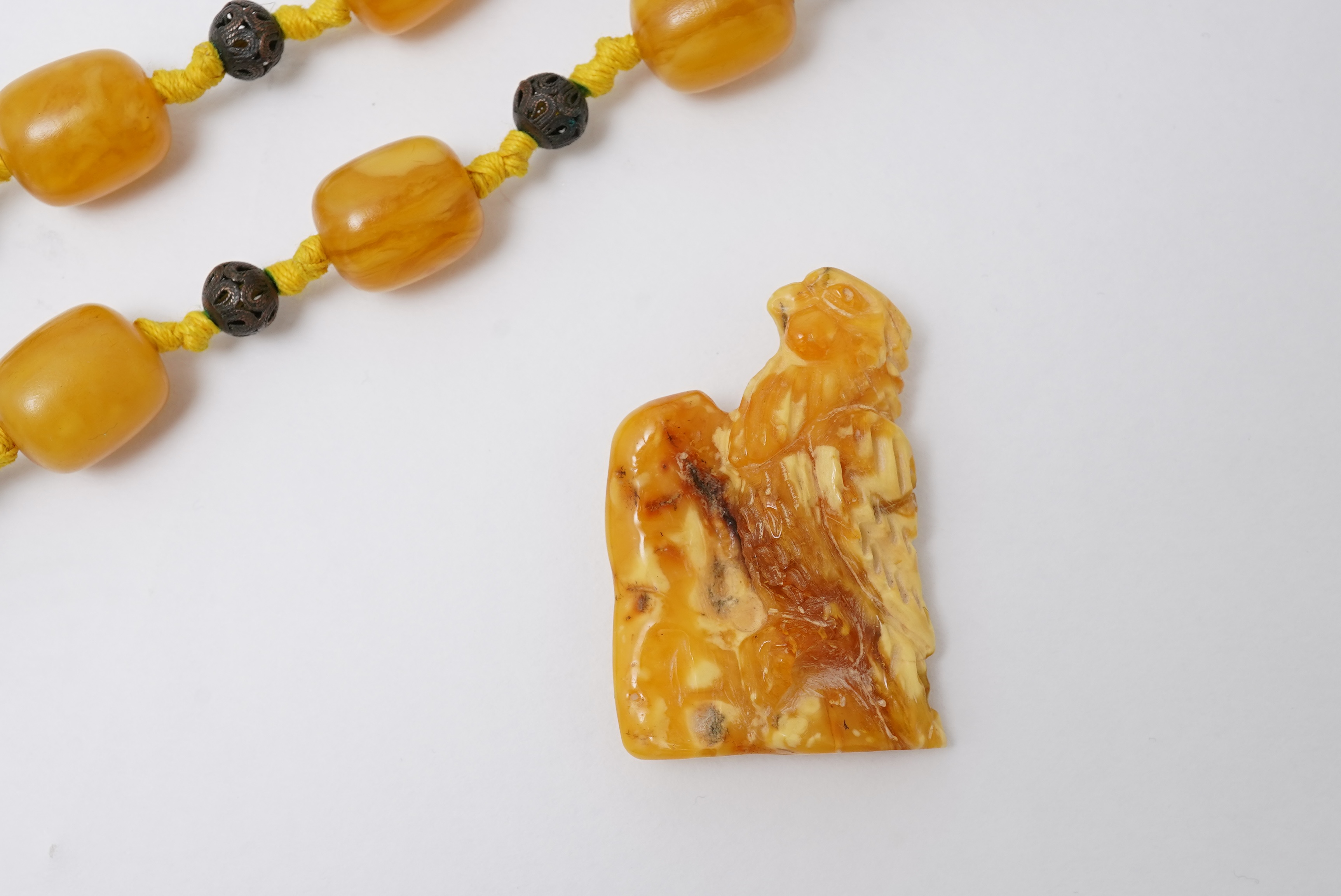An amber necklace and carving, comprising: an amber necklace, composed of beads each measuring approximately 12 x 12 x 14mm, spaced by openwork metal beads, length 48cm; and an amber carving of a hawk on a rock, length 4